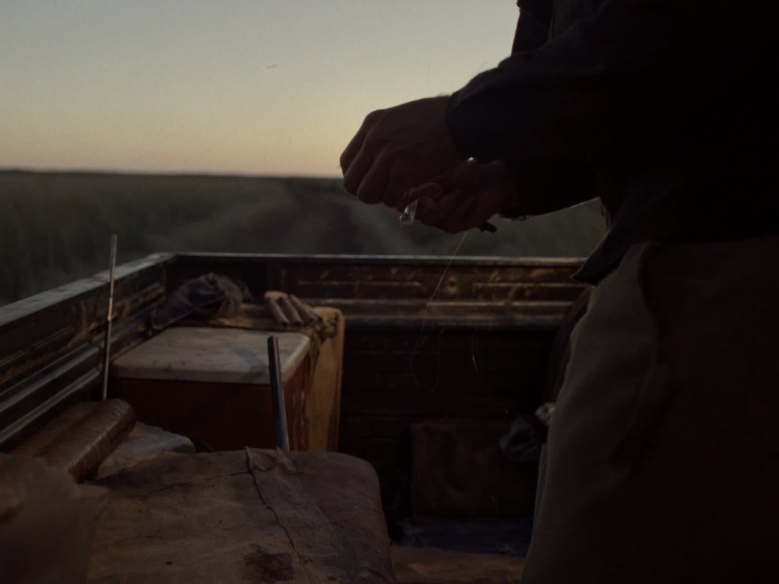 A guide's hands rigging a fly line at the open tailgate of a pickup on a ranch two-track at dawn.