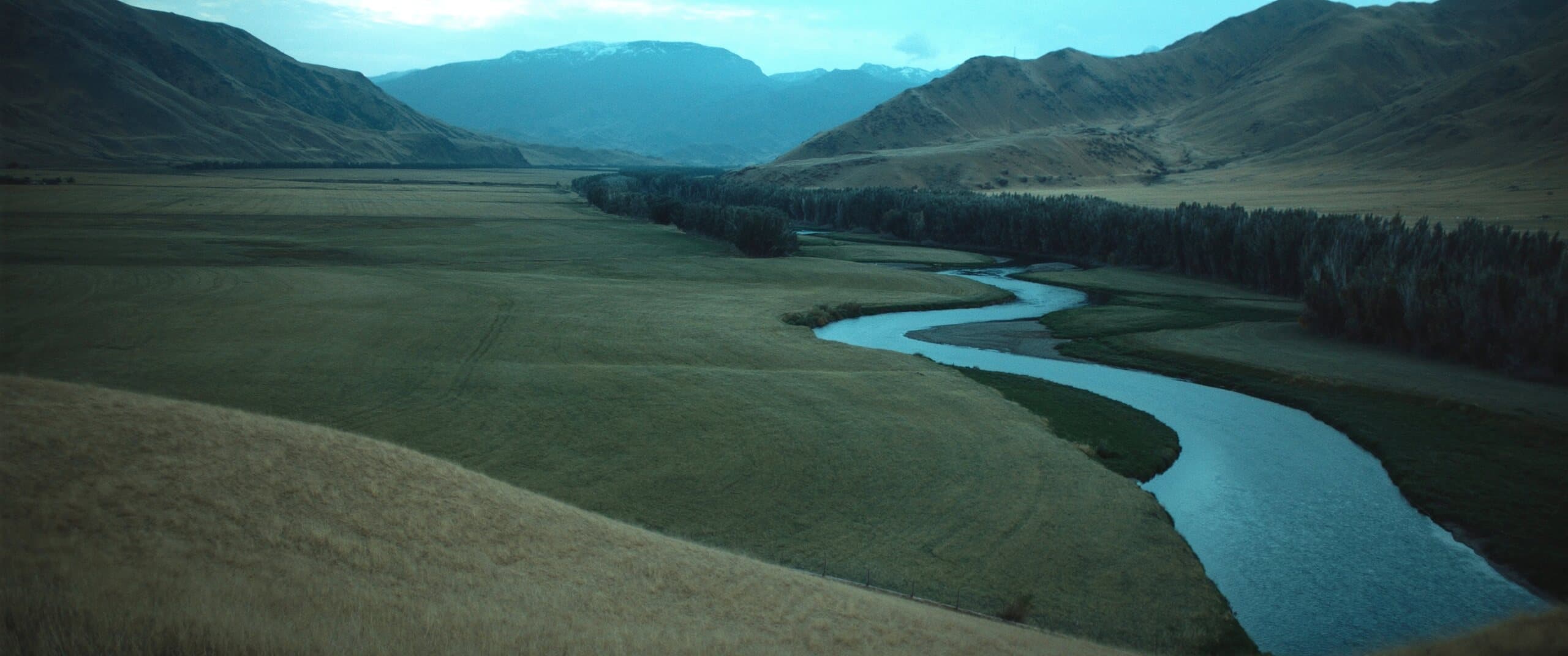 A trout river winding through open ranch grassland toward Western foothills at first light.