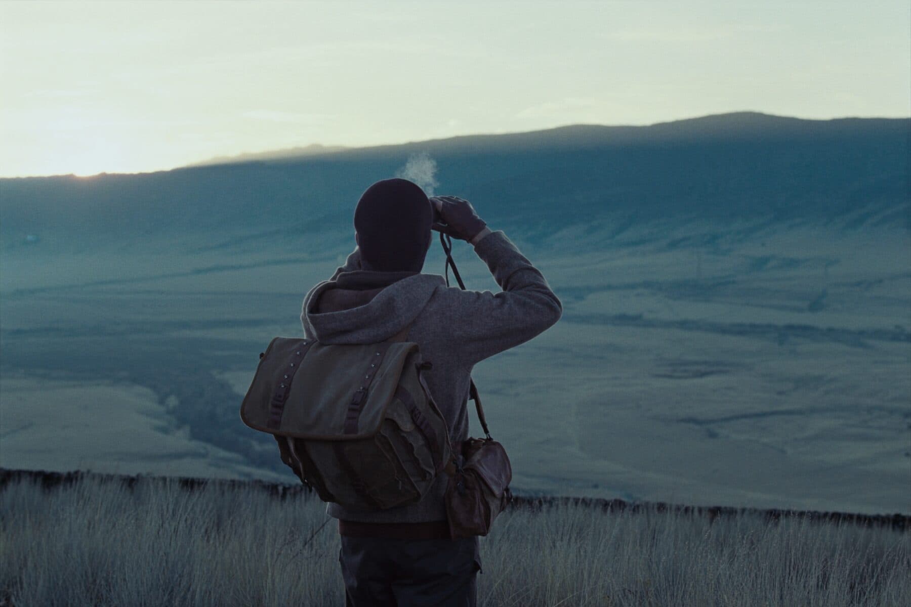 A lone hunter glassing a wide Western basin from a high sagebrush bench at last light.